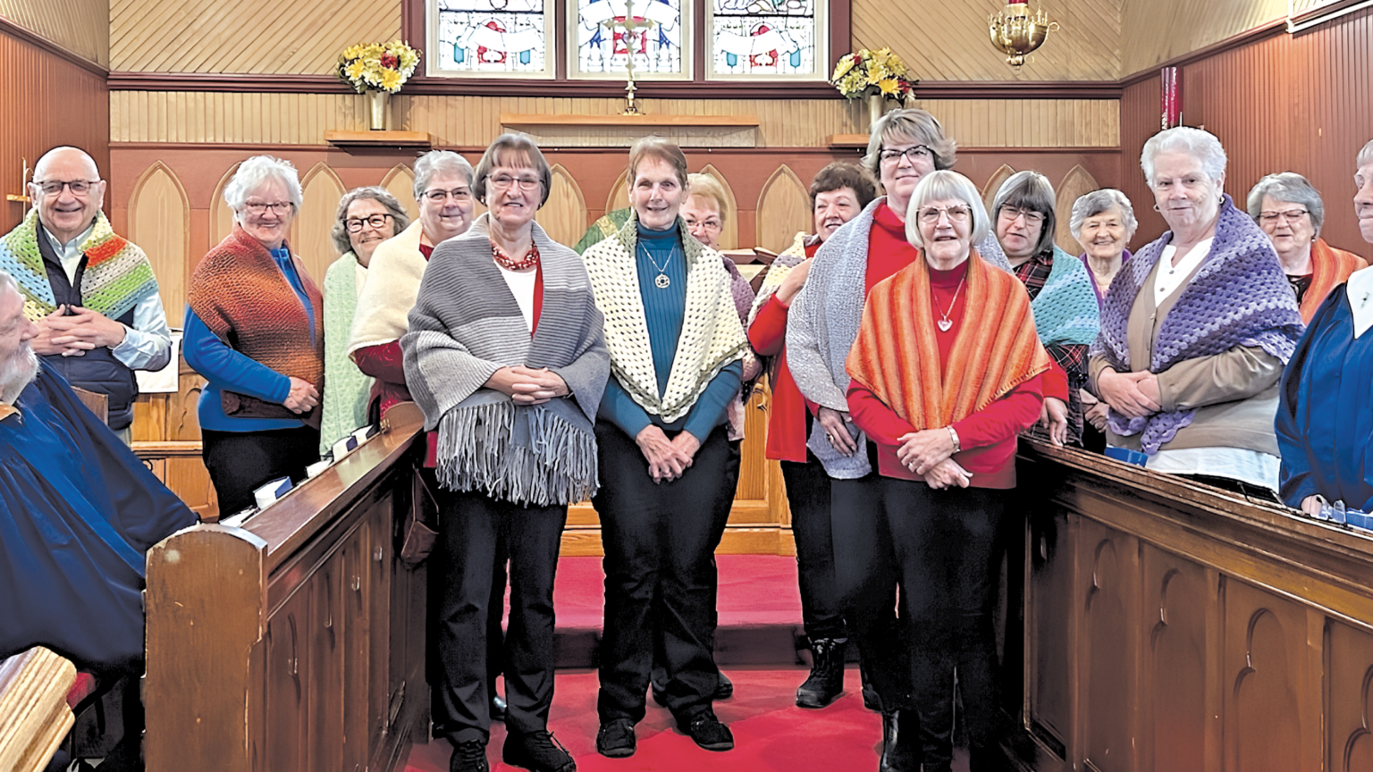 A group of people at the front of a church, wearing prayer shawls that have been recently blessed